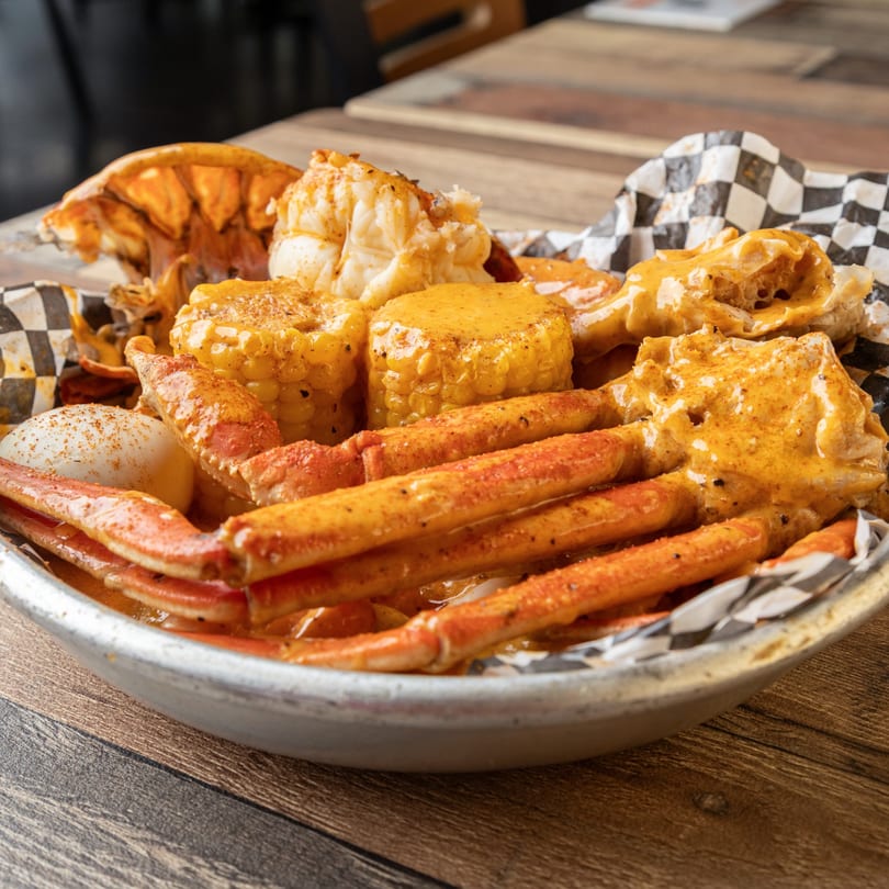 Krustaceans Seafood boil with crab legs, lobster, corn, and potatoes in a metal bowl.