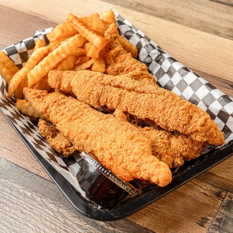 Crispy fried fish fillets and seasoned crinkle-cut fries in a black and white checkered basket.