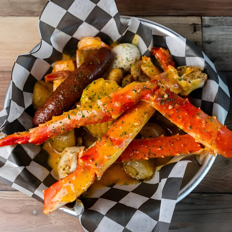 Krustaceans Seafood boil with crab legs, sausage, shrimp, potatoes, and corn in a metal bowl.