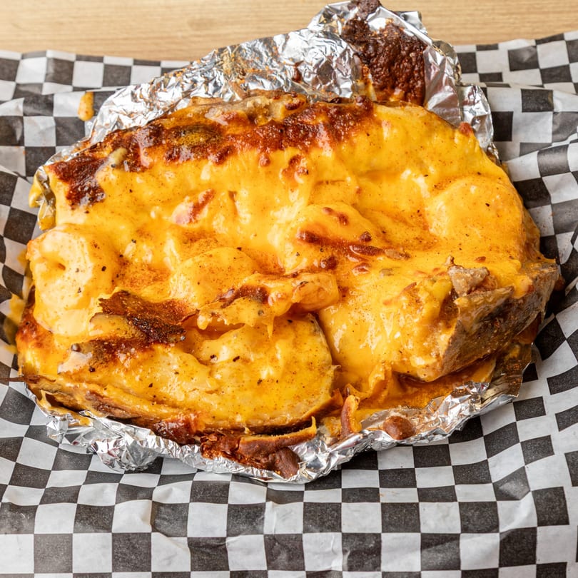 A baked potato topped with melted cheese and shrimp, served in foil on checkered paper.