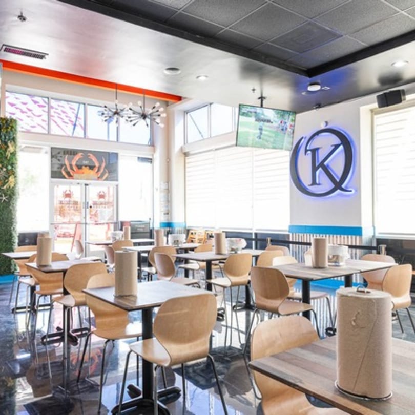 Interior of Krustaceans Seafood restaurant with empty tables, light wood chairs, and a large K logo.