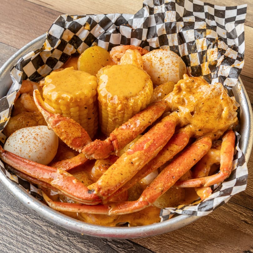 Krustaceans Seafood boil with crab legs, corn, potatoes, shrimp, and eggs in a metal bowl.
