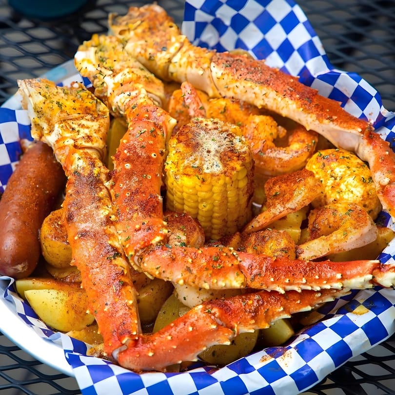 Krustaceans Seafood boil with crab legs, shrimp, corn, sausage, and potatoes in a checkered basket.