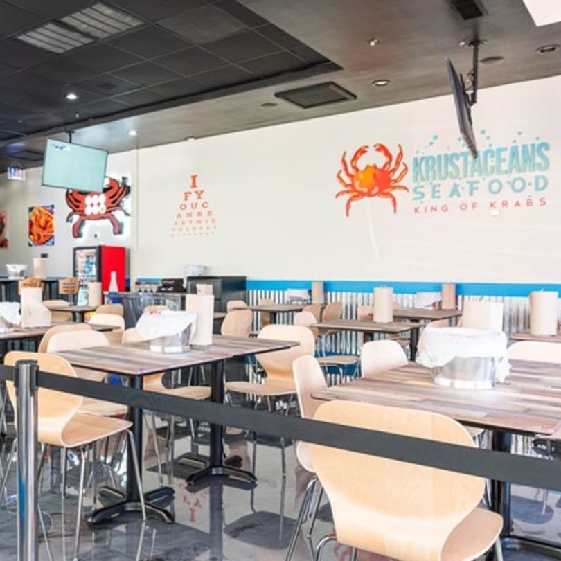 Interior of Krustaceans Seafood restaurant with tables, chairs, and crab-themed wall decor.