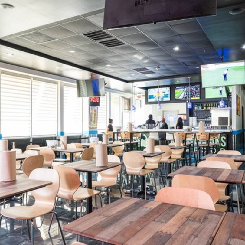 Interior of Krustaceans Seafood restaurant with empty tables, chairs, a bar area, and multiple TVs.